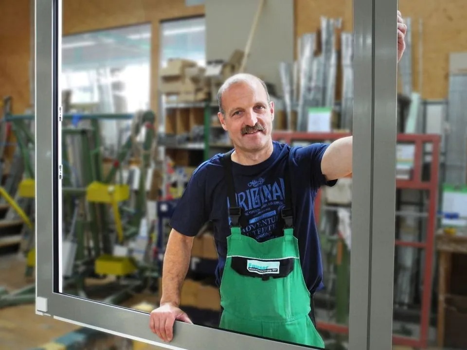Handwerker lächelt durch Fensterrahmen.
